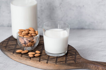 Organic almond milk in a glass bottle next to an almond on a stylish wooden board on a stone table. Natural eco-friendly products.