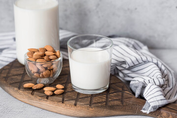 Organic almond milk in a glass bottle next to an almond on a stylish wooden board on a stone table. Natural eco-friendly products.