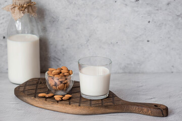 Organic almond milk in a glass bottle next to an almond on a stylish wooden board on a stone table. Natural eco-friendly products.