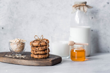 Organic natural cow's milk in a glass bottle, oatmeal, honey and oatmeal cookies on a stylish wooden board on a stone table. Natural eco-friendly products.