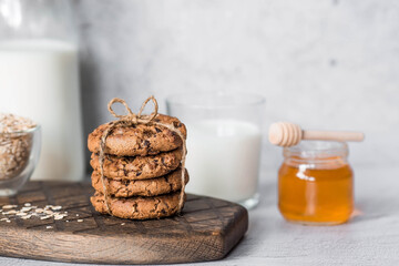 Obraz na płótnie Canvas Organic natural cow's milk in a glass bottle, oatmeal, honey and oatmeal cookies on a stylish wooden board on a stone table. Natural eco-friendly products.