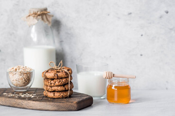 Organic natural cow's milk in a glass bottle, oatmeal, honey and oatmeal cookies on a stylish wooden board on a stone table. Natural eco-friendly products.