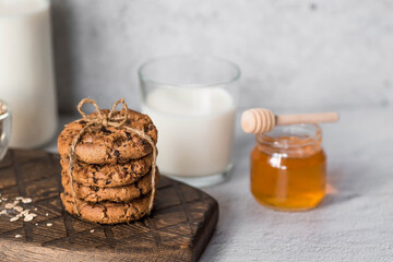 Organic natural cow's milk in a glass bottle, oatmeal, honey and oatmeal cookies on a stylish wooden board on a stone table. Natural eco-friendly products.
