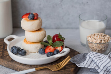 Cottage cheese pancakes, Russian cheesecakes with fresh blueberries, strawberries and mint on a stylish wooden board on a gray concrete table. Natural products. Healthy and delicious breakfast.