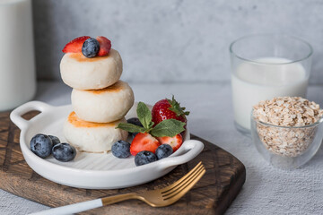Cottage cheese pancakes, Russian cheesecakes with fresh blueberries, strawberries and mint on a stylish wooden board on a gray concrete table. Natural products. Healthy and delicious breakfast.