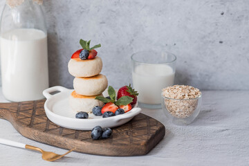 Cottage cheese pancakes, Russian cheesecakes with fresh blueberries, strawberries and mint on a stylish wooden board on a gray concrete table. Natural products. Healthy and delicious breakfast.