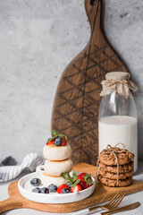 Cottage cheese pancakes, Russian cheesecakes with fresh blueberries, strawberries and mint on a stylish wooden board on a gray concrete table. Natural products. Healthy and delicious breakfast.