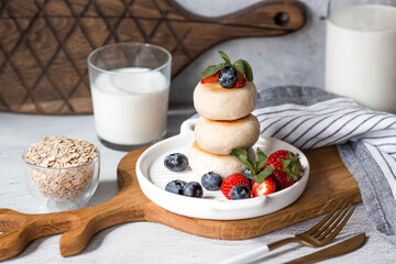 Cottage cheese pancakes, Russian cheesecakes with fresh blueberries, strawberries and mint on a stylish wooden board on a gray concrete table. Natural products. Healthy and delicious breakfast.