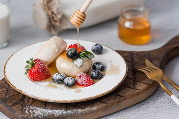 Cottage cheese pancakes,cheesecakes with fresh blueberries, strawberries, honey and mint leaves on a stylish wooden board on a gray concrete table. Natural products. Healthy and delicious breakfast.