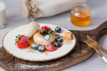 Cottage cheese pancakes,  cheesecakes with fresh blueberries, strawberries, honey and mint leaves on a stylish wooden board on a gray concrete table. Natural products. Healthy and delicious breakfast.