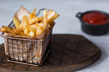French fries in a metal basket with salt and ketchup on a stylish board on a concrete kitchen...