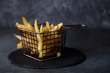 French fries in a metal basket with salt on a stylish board on a dark background. Fried potatoes....