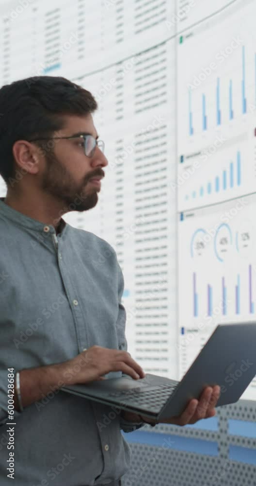 Poster vertical screen: indian man using laptop and standing next to big digital screen with infographics a