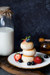 Cottage cheese pancakes, cheesecakes with fresh blueberries, strawberries, honey and mint leaves on a stylish wooden board on a dark background. Natural products. Healthy and delicious breakfast.