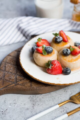 Cottage cheese pancakes, cheesecakes with fresh blueberries, strawberries, honey and mint leaves on a stylish wooden board on a gray concrete table. Natural products. Healthy and delicious breakfast.