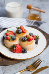 Cottage cheese pancakes, cheesecakes with fresh blueberries, strawberries, honey and mint leaves on a stylish wooden board on a gray concrete table. Natural products. Healthy and delicious breakfast.