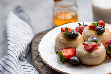 Cottage cheese pancakes, cheesecakes with fresh blueberries, strawberries, honey and mint leaves on a stylish wooden board on a gray concrete table. Natural products. Healthy and delicious breakfast.