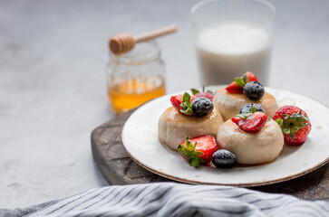 Cottage cheese pancakes, cheesecakes with fresh blueberries, strawberries, honey and mint leaves on a stylish wooden board on a gray concrete table. Natural products. Healthy and delicious breakfast.