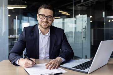 Portrait of successful financier accountant doing paperwork inside office, young man smiling and...
