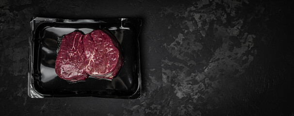 vacuum-packed steak on a dark background. Long banner format. top view