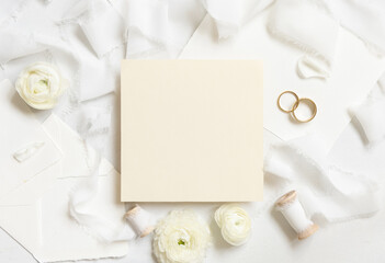 Blank card  near cream roses, white silk ribbons and wedding rings top view, wedding mockup