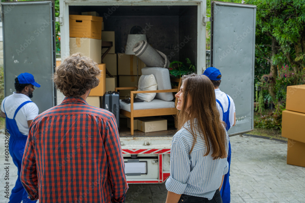 Poster happy couple with moving boxes at new house,moving company employee checks boxes in a truck before s