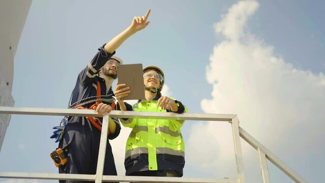 Caucasian engineer man discuss together with co-worker woman hold tablet and standing near wind turbines or windmill ecological energy industry, wind turbine generate electricity