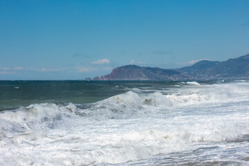 Fototapeta na wymiar Sea waves are not far from the shore with mountains and Alanya city in the distance