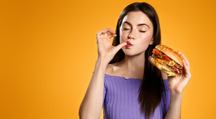 Brunette girl licks her finger, eats tasty hamburger. Woman orders takeaway food with delivery app,...