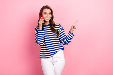 Portrait of funny adorable girl curly hairstyle striped clothes talking on phone directing empty space isolated on pink color background