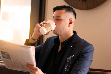 A handsome young businessman sitting in a cafe, drinking coffee and reading newspapers in the...