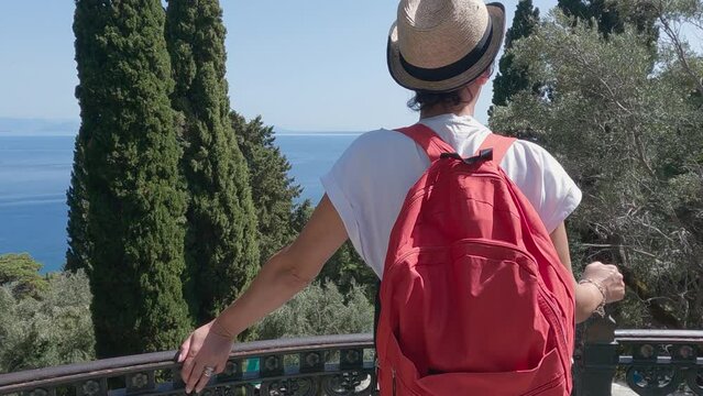 Tourist woman with hat and backpack enjoy the view from the Terrace in the Garden in Achilleion Palace, in Corfu island, Greece, slow motion