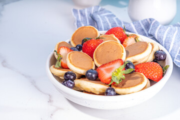 Tiny pancakes with strawberry and blueberry, summer sweet homemade poffertjes breakfast, copy space 