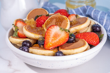 Tiny pancakes with strawberry and blueberry, summer sweet homemade poffertjes breakfast, copy space 