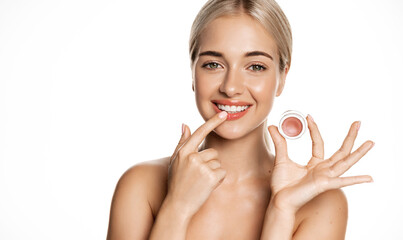 Close up of blond smiling beauty model, girl applies lip balm, pink gloss for natural shine and...
