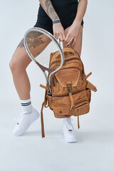 Fototapeta na wymiar Healthy and sportive lifestyle. Sports gear. Bottom view of a female athlete carrying backpack with tennis racket in white background.