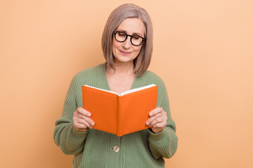 Photo of concentrated smart senior woman with gray hairdo wear khaki cardigan hold book read story isolated on beige color background