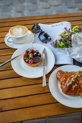 A wooden table with dessert, coffee, utensils, sunglasses, and a magazine