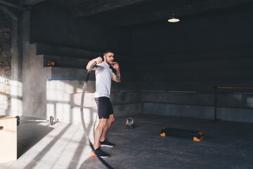 Strong sportsman exercising with battle rope in gym