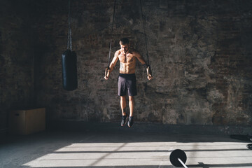 Muscular sportsman doing exercise on gymnastic rings in fitness club
