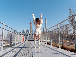 Rear view of beautiful young woman with black long hair in white skirt posing with Shanghai city...