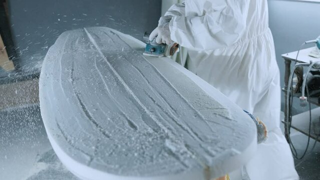 Cropped anonymous professional master polishing surfboard in workshop