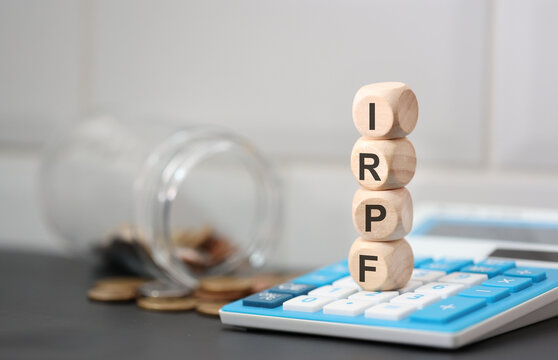 A sigla IRPF para Imposto sobre a Renda das Pessoas F&iacute;sicas escrita em dados de madeira que est&atilde;o sobre uma calculadora. Imposto de Renda no Brasil.