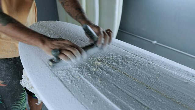 Unrecognizable man polishing surfboard with special tool