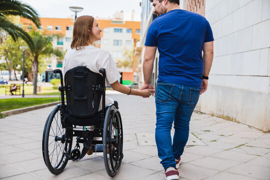 Back view of happy husband with disabled wife walking together on tiled street