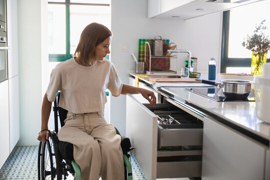 Young woman on wheelchair doing house chores in modern kitchen
