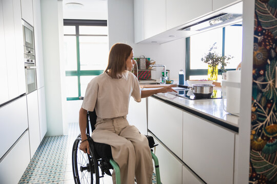 Young woman on wheelchair doing house chores in modern kitchen