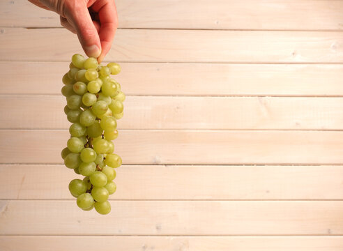 Farmer's hand with green organic grapes on a rustic wooden wall with space for text