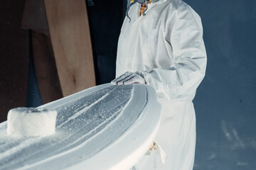 Anonymous man standing near surfboard in workshop