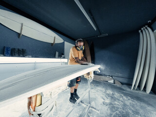 Concentrated man polishing surfboard in workshop